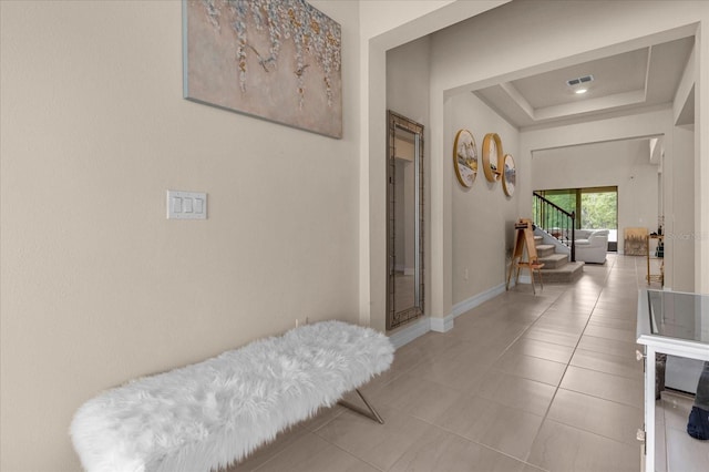 hall with a tray ceiling and light tile patterned floors