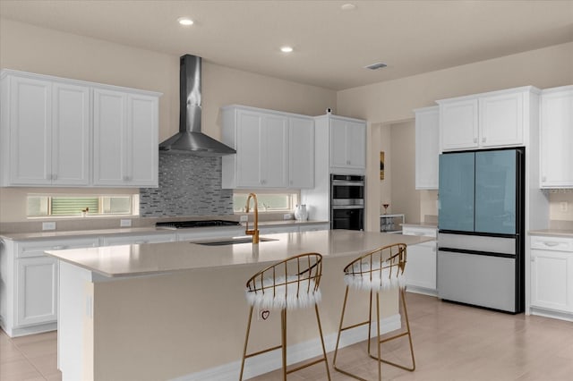 kitchen with a center island with sink, fridge, wall chimney range hood, and white cabinets