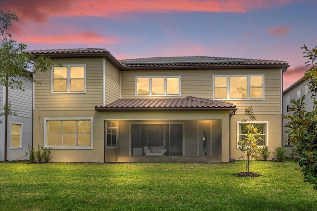 back house at dusk with a sunroom and a lawn