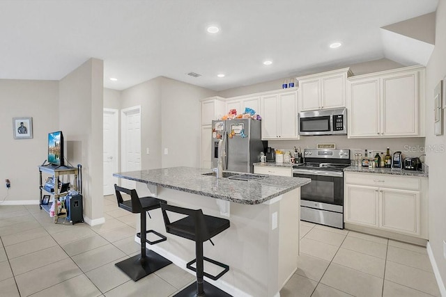 kitchen with stainless steel appliances, an island with sink, light stone countertops, and white cabinetry