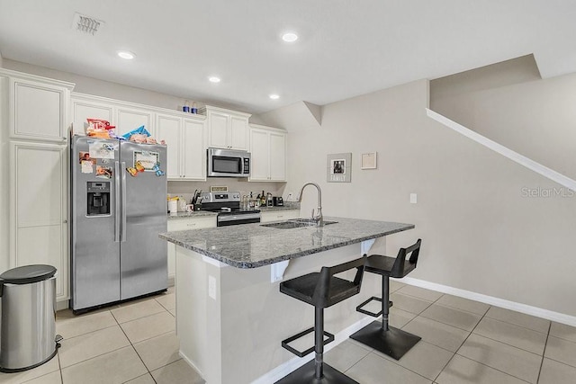 kitchen with white cabinetry, sink, dark stone countertops, light tile patterned floors, and stainless steel appliances