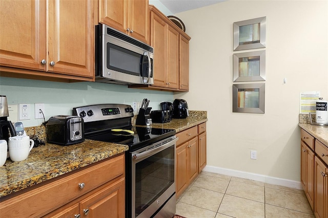 kitchen featuring stainless steel appliances, dark stone countertops, and light tile floors