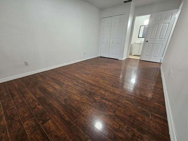 unfurnished bedroom with connected bathroom, a closet, and dark hardwood / wood-style flooring