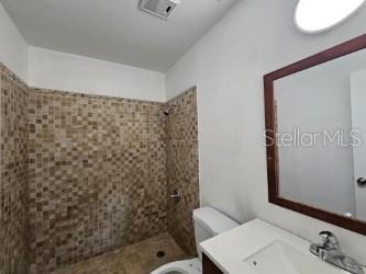 bathroom featuring vanity, toilet, and tiled shower