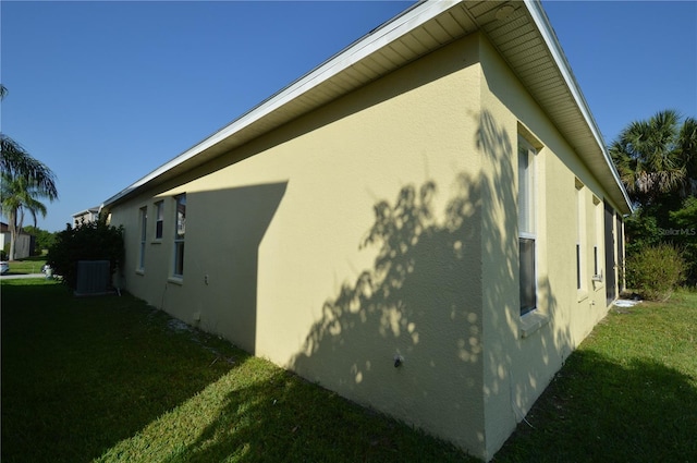 view of side of property with central air condition unit, a yard, and stucco siding