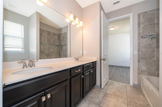 bathroom with wood-type flooring, tiled shower / bath, vanity with extensive cabinet space, and double sink