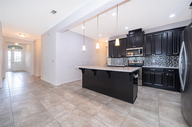 kitchen featuring decorative light fixtures, appliances with stainless steel finishes, sink, a kitchen bar, and an island with sink