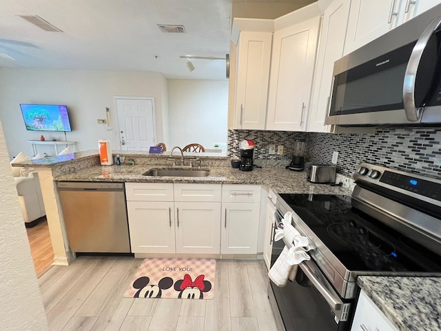 kitchen with light hardwood / wood-style floors, kitchen peninsula, white cabinetry, appliances with stainless steel finishes, and sink