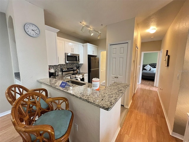 kitchen featuring appliances with stainless steel finishes, tasteful backsplash, rail lighting, and light hardwood / wood-style flooring