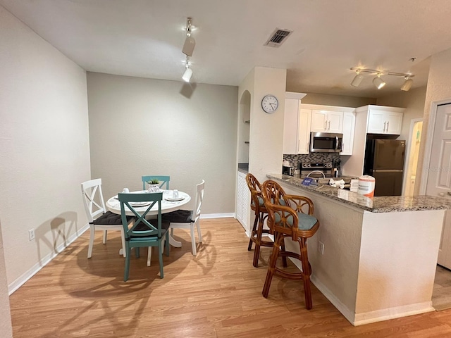 kitchen with light hardwood / wood-style floors, backsplash, track lighting, white cabinetry, and refrigerator