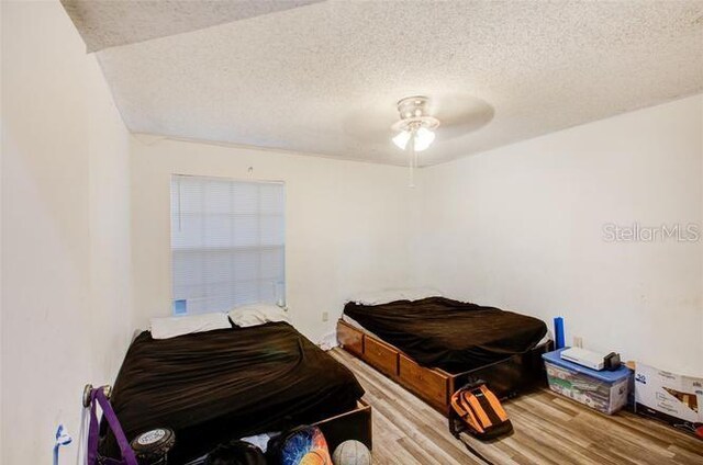 bedroom with a textured ceiling, ceiling fan, and light hardwood / wood-style floors