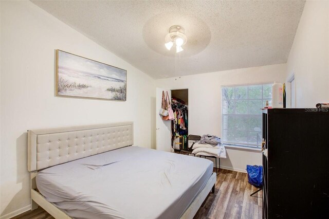 bedroom with a closet, vaulted ceiling, hardwood / wood-style flooring, ceiling fan, and a textured ceiling