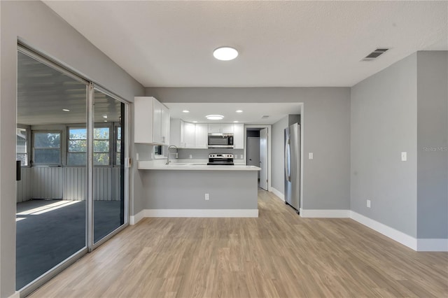 kitchen featuring appliances with stainless steel finishes, kitchen peninsula, white cabinetry, and light hardwood / wood-style flooring