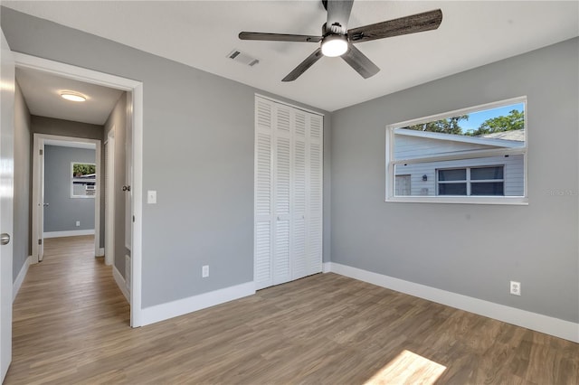 unfurnished bedroom featuring wood-type flooring, ceiling fan, multiple windows, and a closet