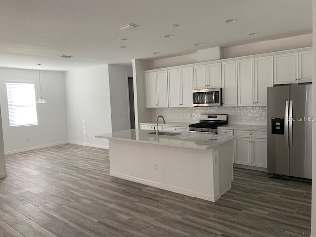 kitchen with sink, white cabinetry, hanging light fixtures, stainless steel appliances, and a kitchen island with sink