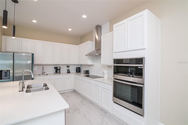 kitchen featuring decorative light fixtures, stainless steel appliances, wall chimney exhaust hood, white cabinets, and sink