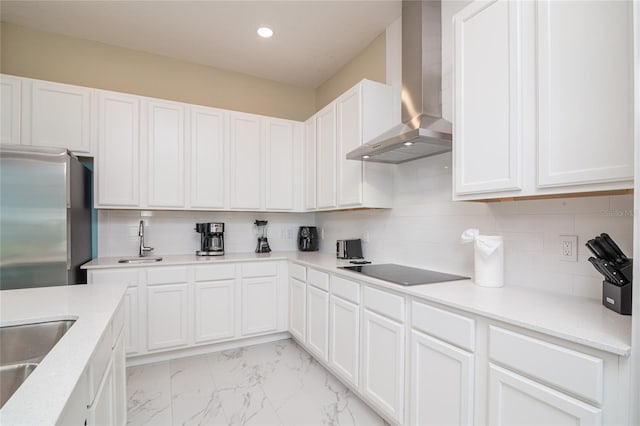 kitchen featuring backsplash, wall chimney range hood, white cabinets, and stainless steel refrigerator