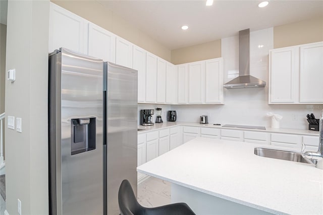 kitchen featuring stainless steel fridge with ice dispenser, wall chimney exhaust hood, white cabinetry, a kitchen breakfast bar, and black electric stovetop