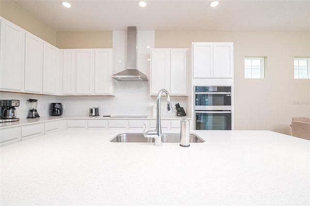 kitchen with white cabinets, sink, wall chimney range hood, and double oven