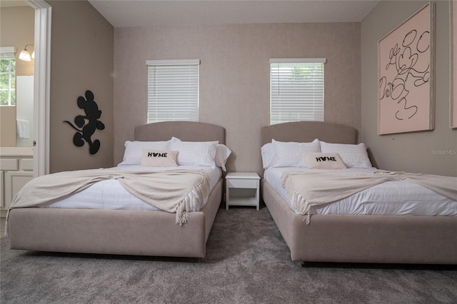 bedroom with multiple windows, dark carpet, and ensuite bathroom