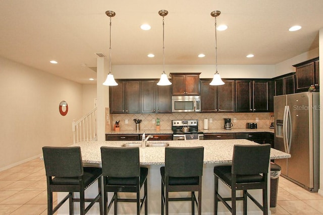 kitchen with pendant lighting, sink, light tile patterned flooring, a kitchen island with sink, and stainless steel appliances