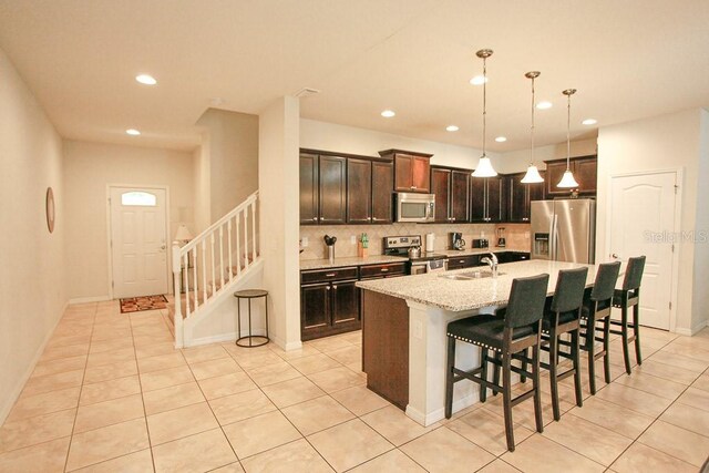 kitchen with hanging light fixtures, sink, light tile patterned flooring, a kitchen island with sink, and stainless steel appliances