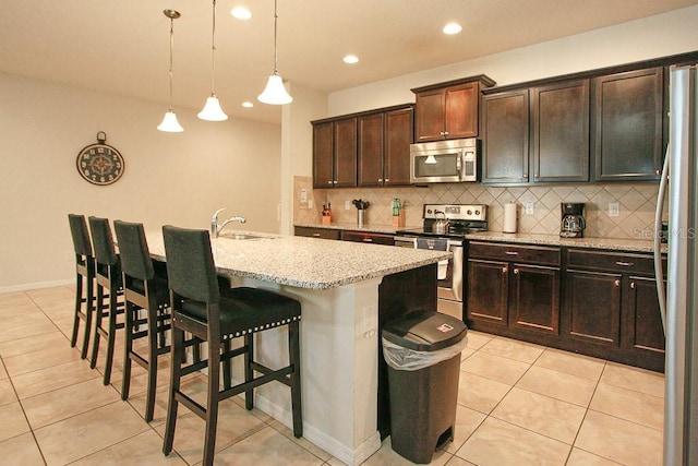 kitchen with appliances with stainless steel finishes, decorative light fixtures, sink, light stone countertops, and a kitchen island with sink