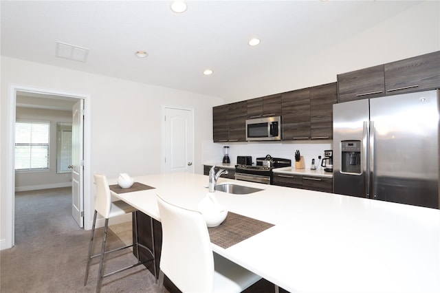 kitchen with appliances with stainless steel finishes, sink, a breakfast bar area, dark brown cabinets, and carpet floors