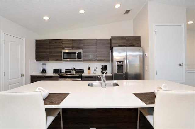 kitchen featuring dark brown cabinetry, sink, tasteful backsplash, stainless steel appliances, and vaulted ceiling