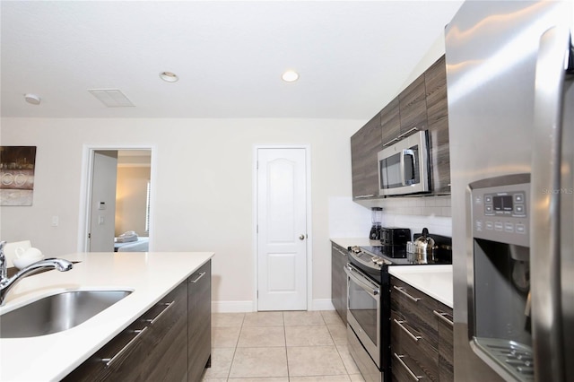 kitchen featuring appliances with stainless steel finishes, dark brown cabinets, light tile floors, sink, and tasteful backsplash