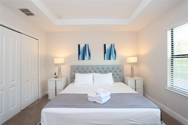 bedroom with dark carpet, a closet, and a tray ceiling