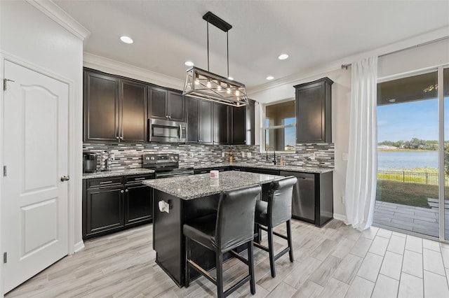 kitchen with pendant lighting, stainless steel appliances, a center island, a water view, and light stone countertops