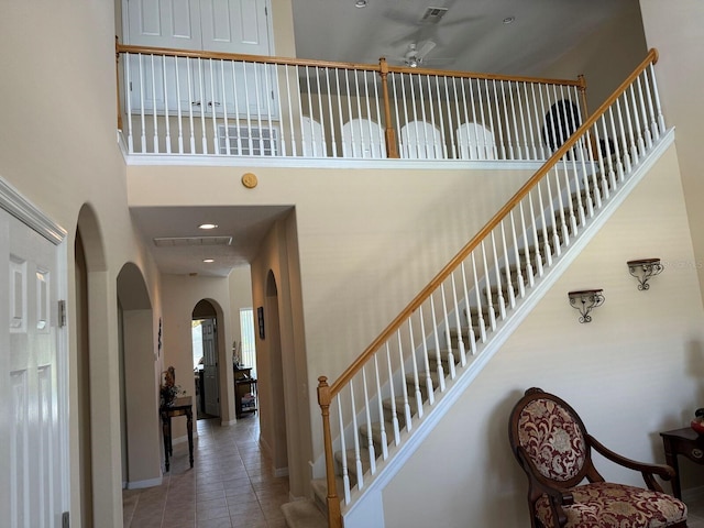 staircase featuring ceiling fan, tile patterned flooring, and a towering ceiling