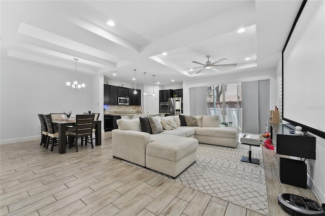 living room with ceiling fan with notable chandelier, a tray ceiling, light wood-type flooring, and sink