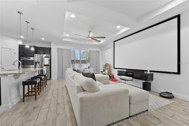 home theater with a raised ceiling, ceiling fan, light wood-type flooring, and sink