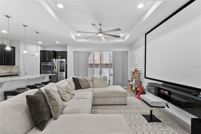 home theater room with a tray ceiling, sink, and ceiling fan