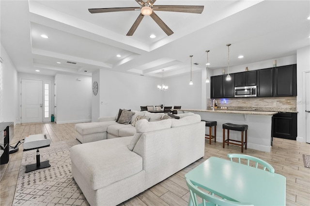 living room with a tray ceiling, ceiling fan with notable chandelier, light hardwood / wood-style floors, and sink