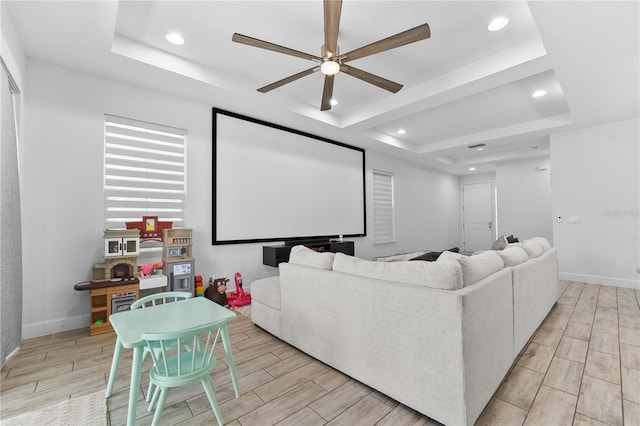 cinema featuring light wood-type flooring, a tray ceiling, and ceiling fan