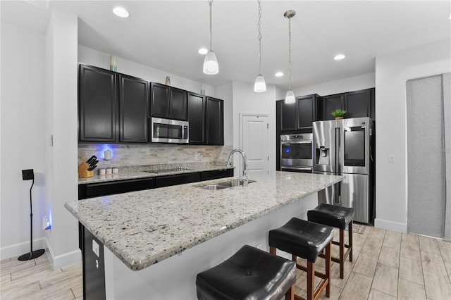 kitchen with appliances with stainless steel finishes, a kitchen island with sink, decorative light fixtures, backsplash, and sink