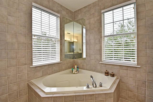 bathroom with a healthy amount of sunlight, tiled tub, and tile walls