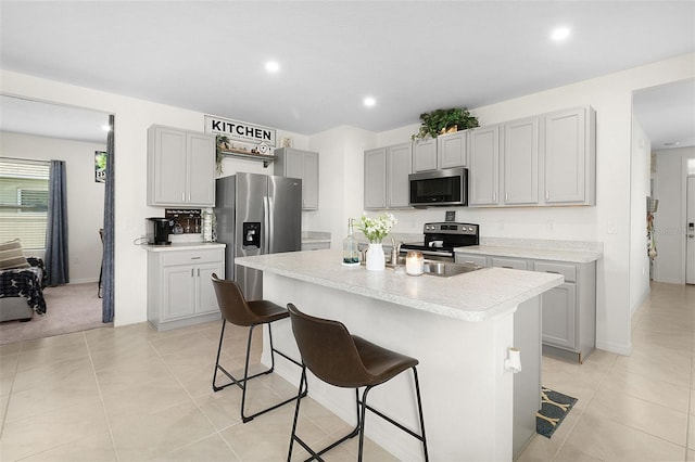 kitchen with stainless steel appliances, a breakfast bar, a kitchen island, and light tile floors