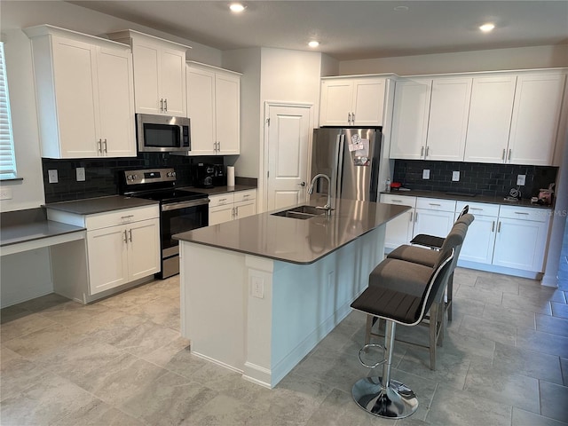 kitchen featuring white cabinets, backsplash, stainless steel appliances, sink, and an island with sink