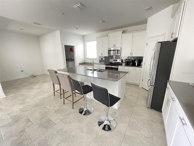 kitchen featuring appliances with stainless steel finishes, a kitchen island with sink, washer / clothes dryer, white cabinetry, and sink