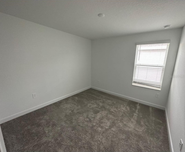 empty room featuring a textured ceiling and dark carpet