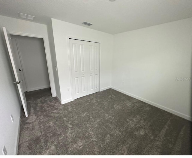 unfurnished bedroom with dark colored carpet and a closet