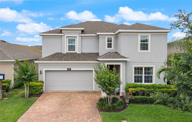 traditional-style house with stucco siding, decorative driveway, roof with shingles, and a front lawn