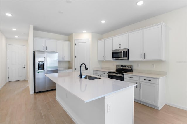 kitchen with appliances with stainless steel finishes, a kitchen island with sink, sink, and white cabinets