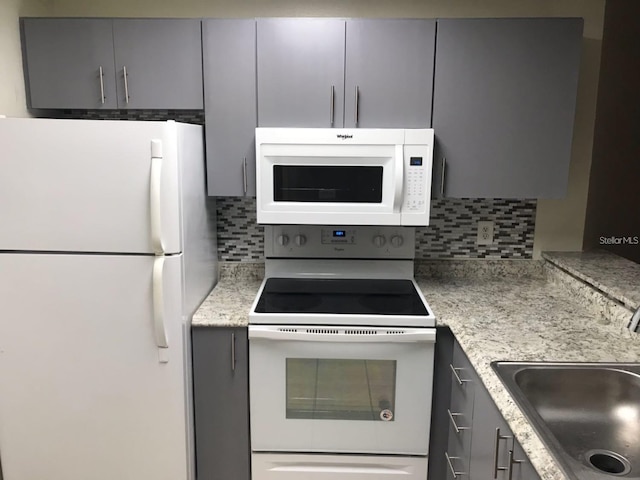 kitchen with light stone countertops, gray cabinetry, white appliances, backsplash, and sink