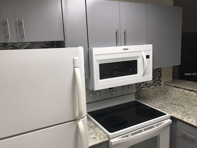 kitchen with light stone countertops, gray cabinets, white appliances, and backsplash