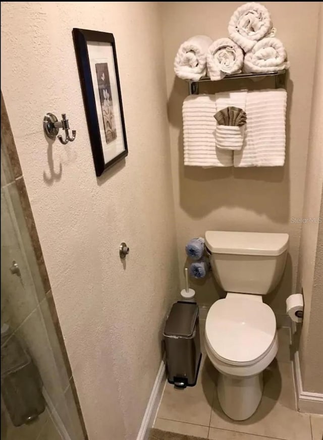 bathroom with walk in shower, toilet, and tile patterned flooring